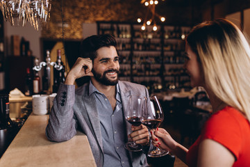 Attractive young couple clinking by wine glasses in restaurant during date.