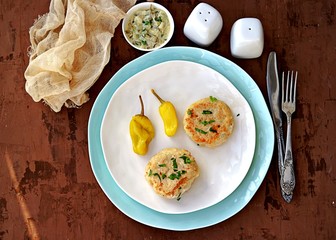 Homemade fish cakes on a white plate. Served with tartar sauce of mayonnaise and grated pickled cucumber, and marinated hot pepper.