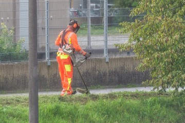 Gärtner mäht das Gras einer Böschung in einer Stadt mit einem Akku Rasentrimmer, Deutschland