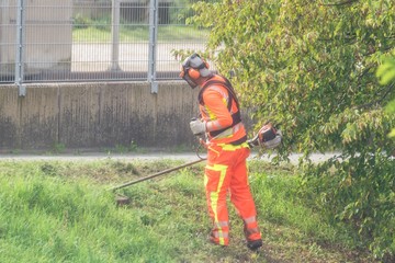 Gärtner mäht das Gras einer Böschung in einer Stadt mit einem Akku Rasentrimmer, Deutschland