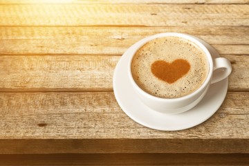 Coffee with heart shaped foam on wooden background