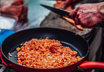 Red Pan with Pile of Cut Salmon Pieces in the Foreground, Male Chef Cutting Fresh Salmon on the Wooden Board in the Background - Isolated Action with Only Hands Showing, Kitchen Set