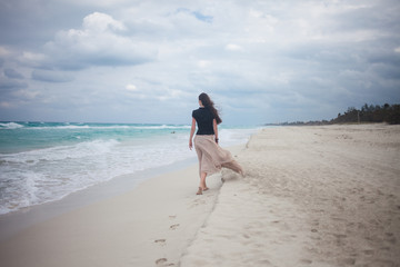 young woman in a long skirt walking on the ocean. 