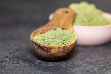 Powdered matcha in bowl and wooden spoon on dark background - medicine alternative