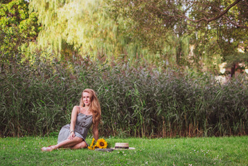 Beautiful woman with long blond hair walking in the park with sunflowers bouquet, green grass, summertime