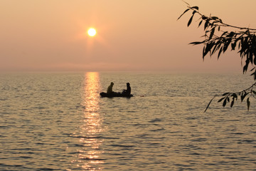 Naklejka na ściany i meble fishermen in a boat on the lake at sunset in the evening