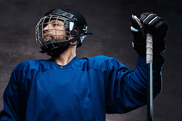 Portrait of a bearded ice-hockey player in a blue sportswear with gaming stick. Studio shot.