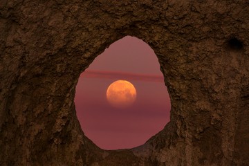 Sunset moon through a hole in the mountain 