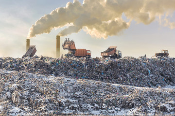 Dump trucks unloading garbage over vast landfill. Smoking industrial stacks on background. Environmental pollution. Outdated method of waste disposal. Survival of times past - obrazy, fototapety, plakaty