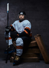 Portrait of a bearded hockey player wearing full sports equipment holding a hockey stick while...