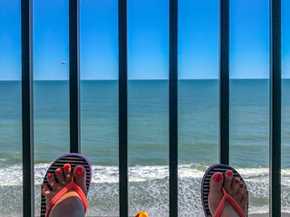 two female feet with a pedicure against the background of the ocean beachfront boardwalk Myrtle...