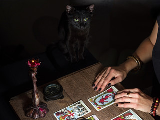 The fortune teller lays out on a wooden table the tarot cards by the light of a lantern and a...