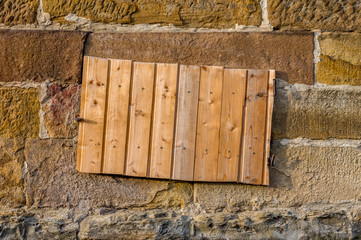 Sandsteinmauer mit Kellerfenster und Schacht für Kartoffel oder Kohlekeller, abgedeckt mit Brett aus Holzpaneelen, Nahaufnahme