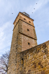 Fototapeta na wymiar Wehrturm mit Zwiebeldach aus Schieferschindeln und Stadtmauer einer Stadtbefestigung aus Sandstein bei bedecktem Himmel und vier fliegende Vögel