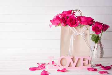 Valentines day and love concept. Pink roses in paper bag with Wooden letters forming word LOVE written on white wooden background.