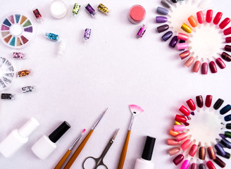 A set of cosmetic tools for manicure and pedicure on a weyt background. Gel polishes, nail files and clippers, and the lamp top view. Composition for card with a place for text