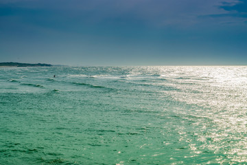 Obraz premium View of the beautiful scenic sea, reflecting sun, dark storm clouds and two people swimming in the distance on a paddle board.North sea in France.