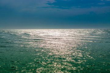 View of the picturesque sea, bright sun reflection and dark stormy sky.