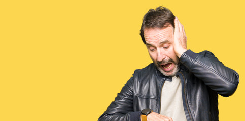 Middle age handsome man wearing black leather jacket Looking at the watch time worried, afraid of...