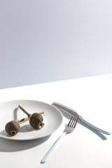 White plate, cutlery and dry poppy on a plate on a bright table. Cretive minimalistic concept.