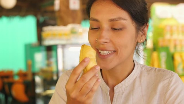 Young Tourist Woman Trying Durian First Time. Female Holding Piece of Durian Pulp and Sniffing It Enjoying Good Sweet Smell. 4K Slowmotion. Kuala Lumpur, Malaysia.
