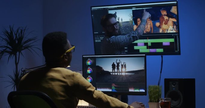 Medium shot of a young man editing video inside the room while his colleague is giving instructions