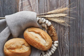 Bread buns in basket on rustic wood with wheat ears