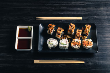 Sushi rolls with chopsticks and soy sauce on dark background. Top view