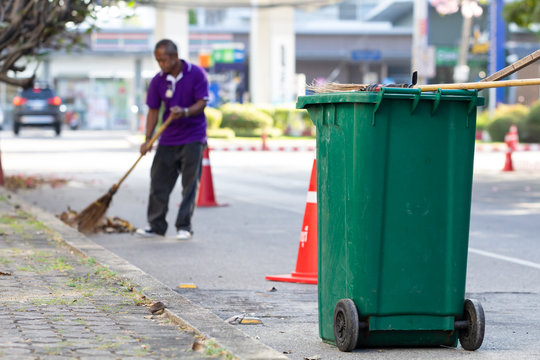 Green trash bin with cleaning worker sweeping garbage.