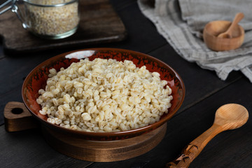 Pearl barley porridge in a plate on a black wooden background