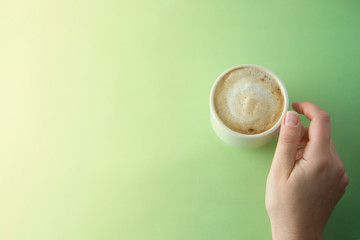 Female hands holding a cup of coffee with foam over green background. Flat lay.