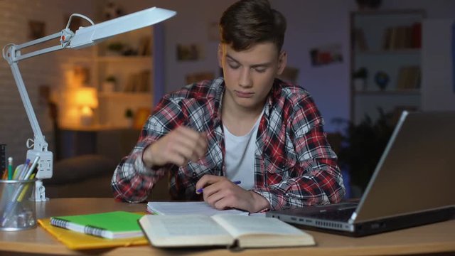 Left-handed overloaded teenage student preparing for examination, feeling sleepy