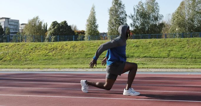 A black man in the hood is training at the stadium before running.