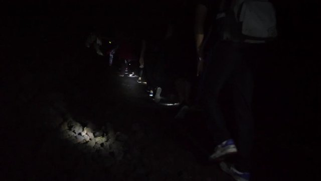 Group of Young Tourists with Flashlights Walking on Path at Night to the Top of Batur Volcano to See Amazing Sunrise. 4K Slowmotion POV Travel Active Lifestyle Concept. Bali, Indonesia.