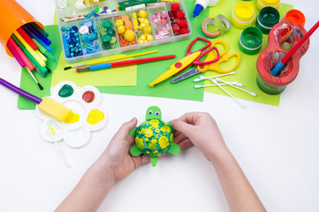 The child makes a craft toy from foam plastic tortoise. Material for creativity and education.