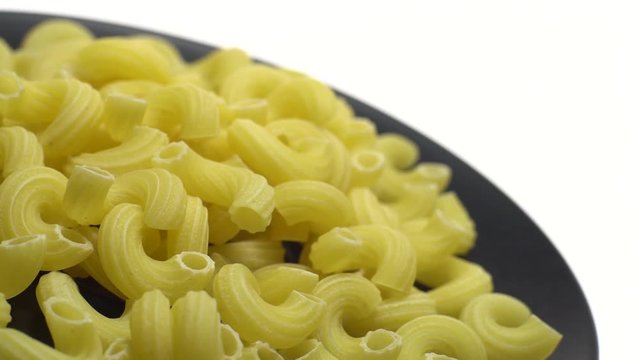 Raw macaroni in rotation. Elbow macaroni.  Macaroni rigati close up.  Raw pasta  isolated on white. Italian cuisine concept.