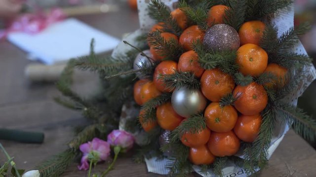 Slow shot of the winter bouquet in the foreground. Bouguet is very big and non-standart with mandarines, christmas toys and sprigs of fir trees.
