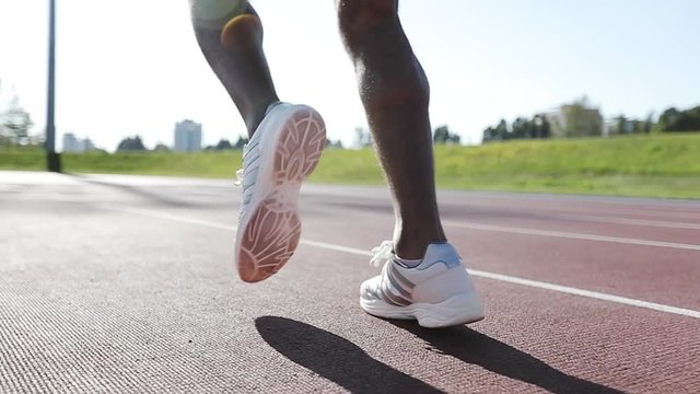 Close-up of the feet of a black man running in an outdoor stadium.