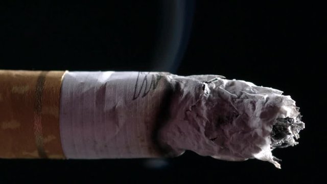 Cigarette burning in front of a black background. Extreme macro close up in Slow-motion.