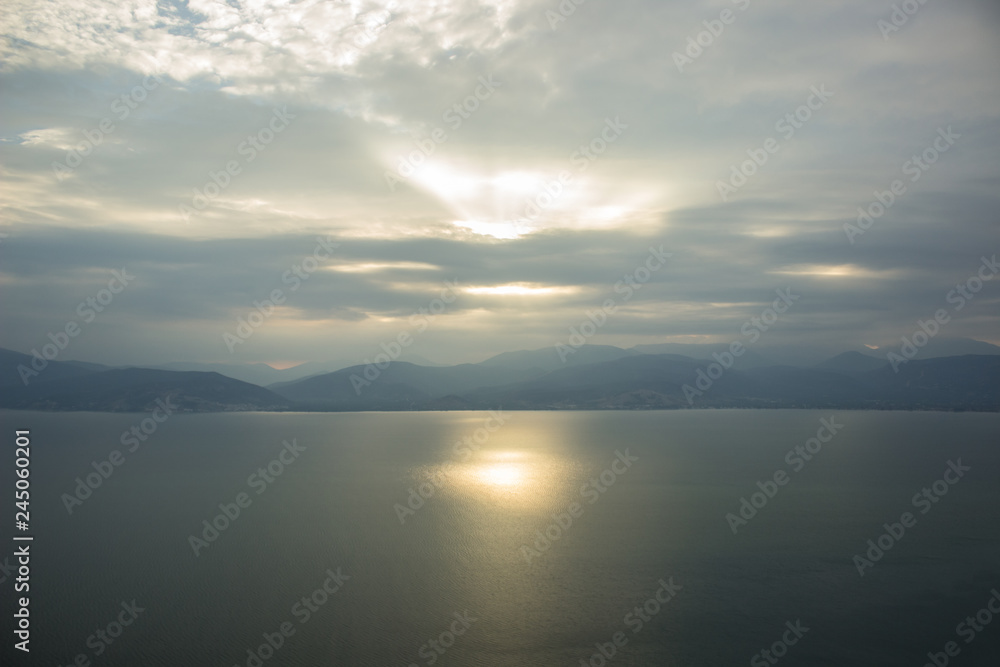 Poster gray rainy and cloudy weather background landscape of morning sun rise time above lake calm water surface with mountain horizon silhouettes