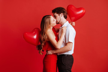 Portrait of attractive young couple posing on red background and holding balloons heart. Valentine's day.