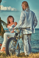 Naklejka premium Young romantic couple with vintage custom motorbike on the tropical coast background.