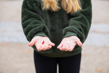 Unrecognizable young female demonstrating two different medical pills in hands while standing in park