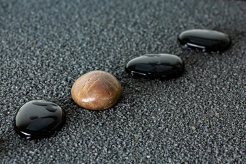 Black pebbles on black sand background with brown pebble.