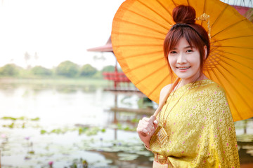 Asian girl Wearing traditional Thai clothes Holding a yellow sun shade Stroll along the lotus pond