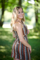 Fototapeta premium Stunning young blonde woman in summer dress standing in shady area of park