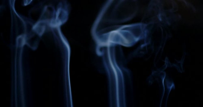 Bluish cloud of smoke or vapor rises against a black background in slow motion