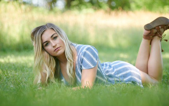 Stunning young blonde woman in summer dress laying on stomach in grass in shade
