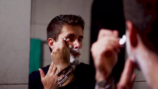 Handsome man shaving in mirror with double edge razor