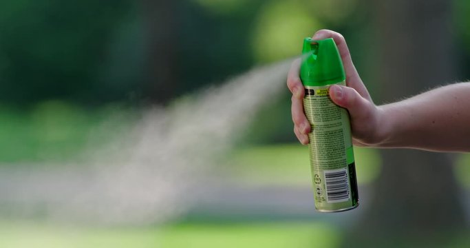Medium shot of hand spraying mosquito insect repellent aerosol can in slow motion